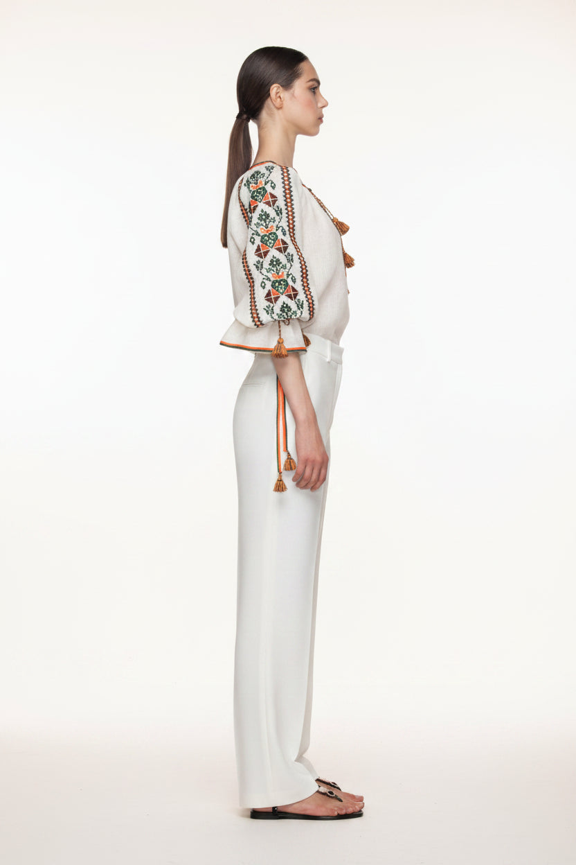 Woman wearing a white outfit with floral embroidery and tassels on a white background, Foberini brand visible.
