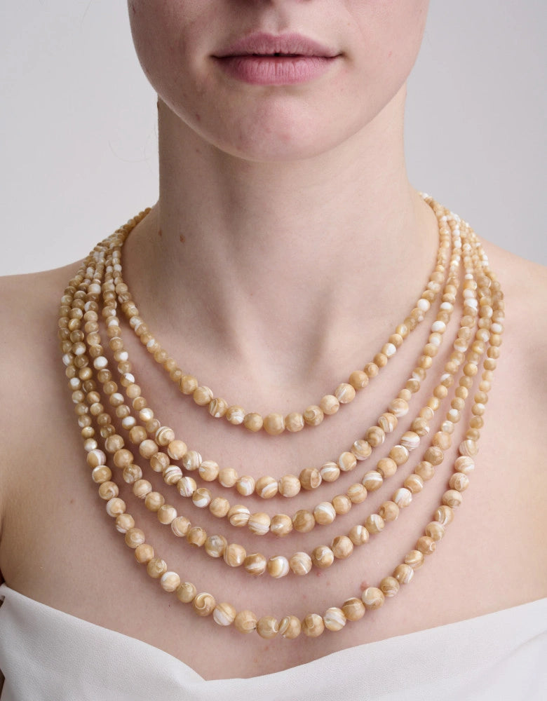 Close-up of a person wearing multiple layered pearl necklaces against a neutral background