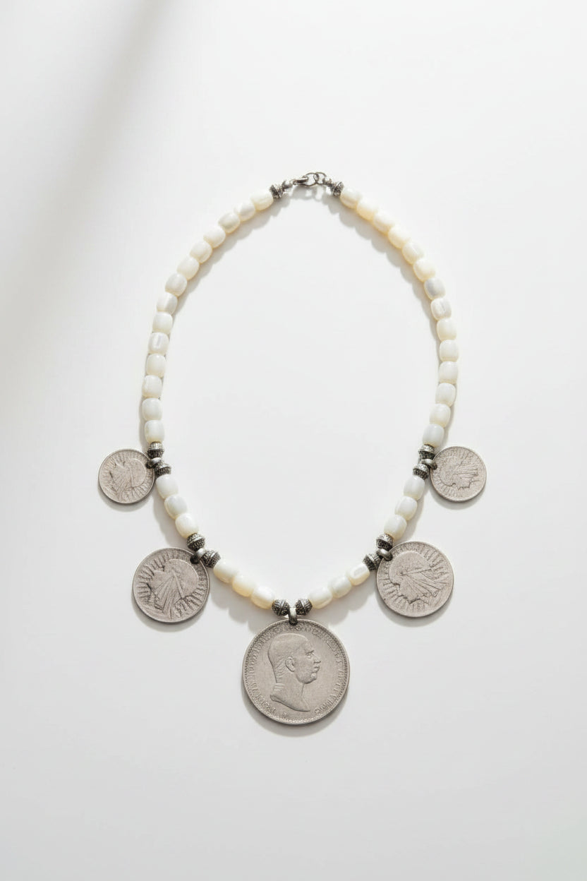 A beaded necklace with white round beads and several silver coin charms, Traditional zgărzi often used vibrant, opaque glass beads (red, blue, green, or black) in geometric woven patterns. The choice of light-colored, pearlescent beads is a modern adaptation—it adds a soft, luminous quality that complements the cool patina of antique silver without overpowering the coins.