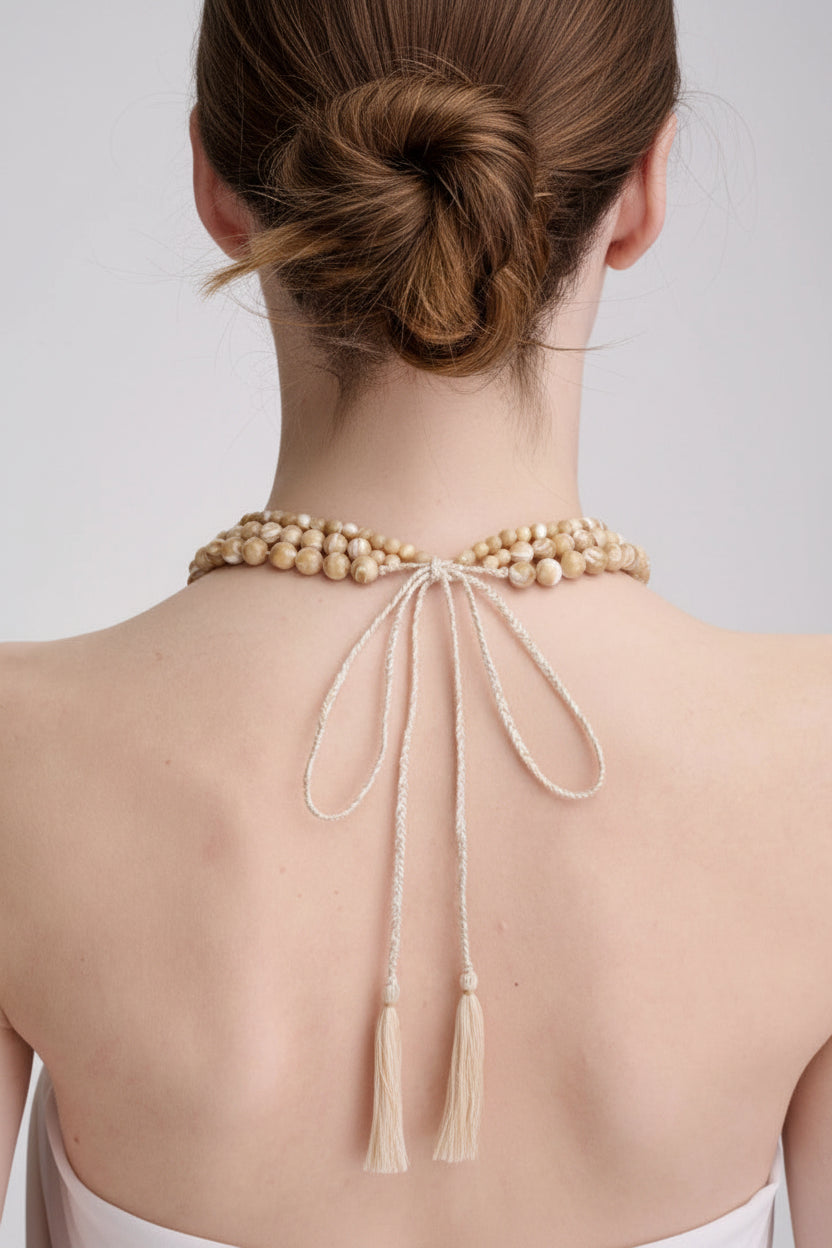 Beige beaded halter top with tassels on a plain background