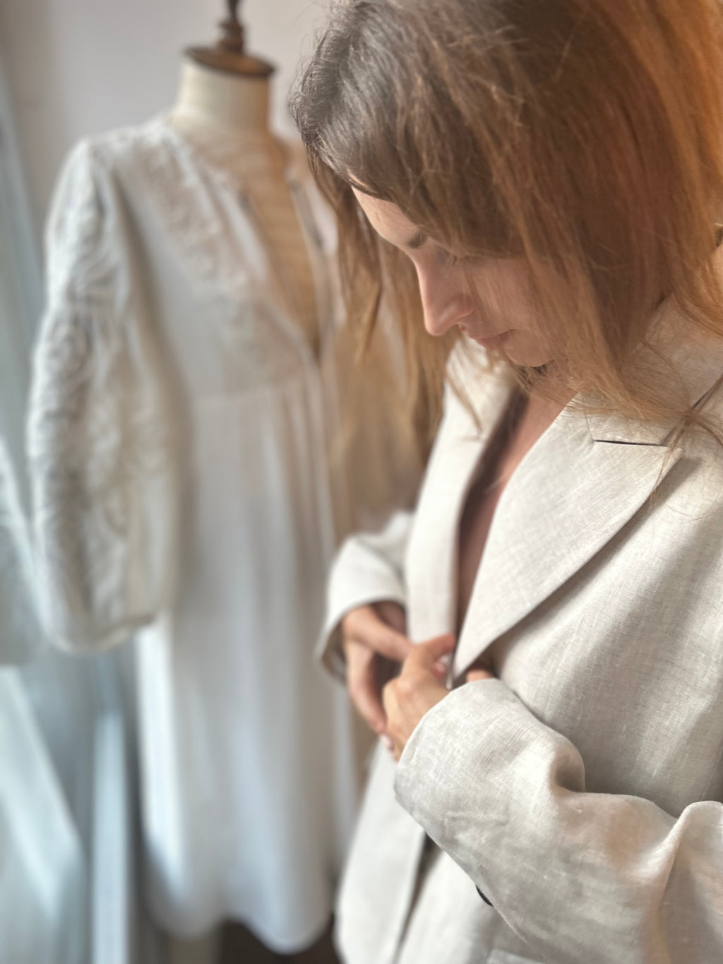 Woman adjusting a light-colored blazer on a mannequin in a clothing store.