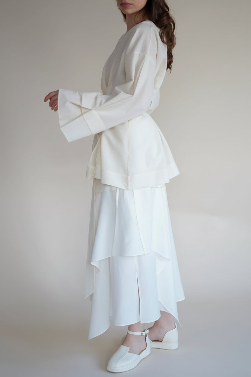 Woman wearing a white outfit with long sleeves and layered skirt against a plain background