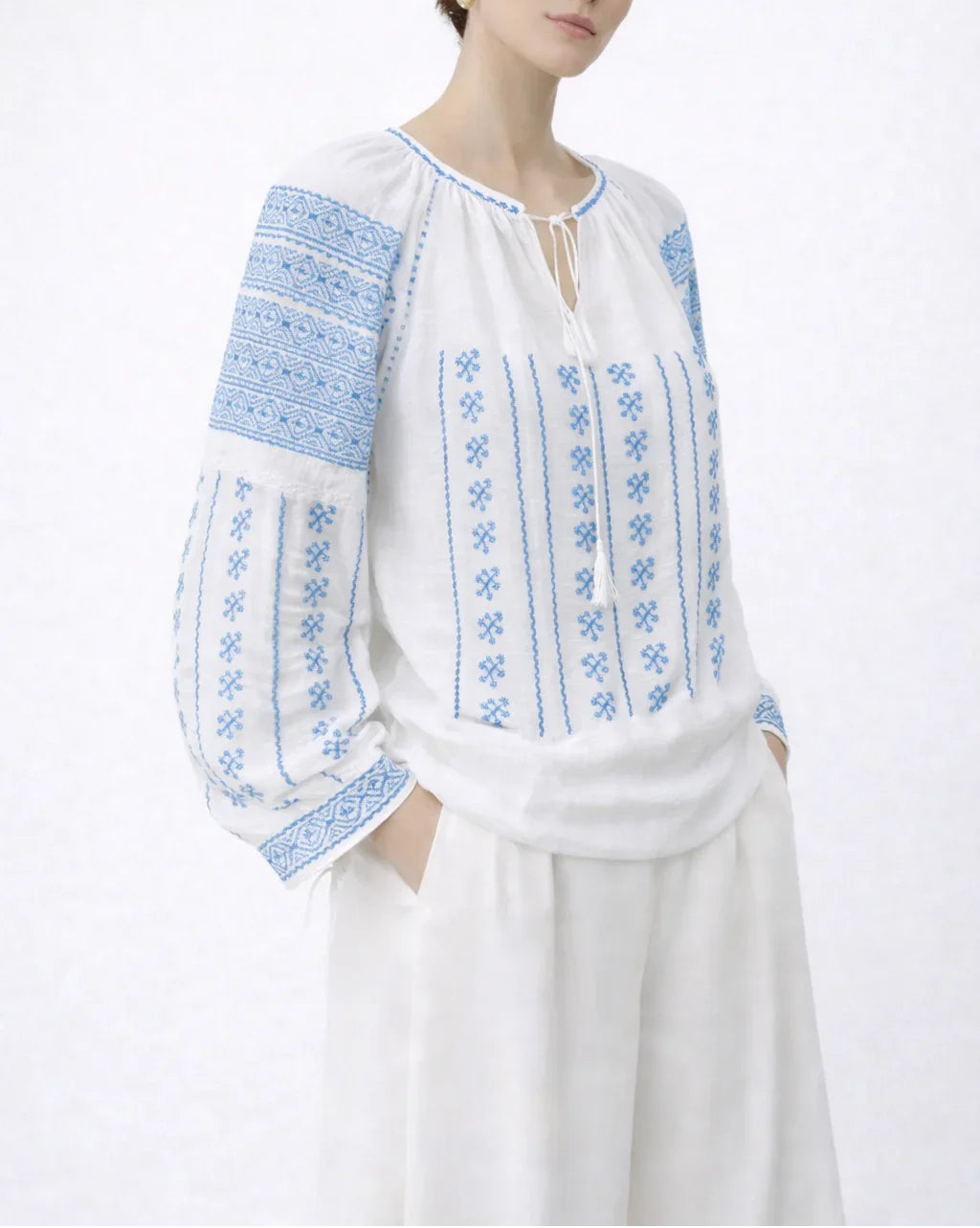 Woman wearing a white blouse with blue embroidery on a white background