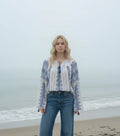 Woman standing on a beach wearing a patterned blouse and jeans with a foggy ocean background.