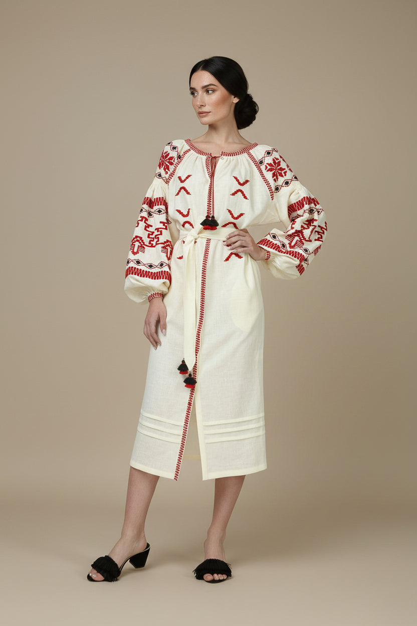 Woman wearing a cream dress with red embroidery against a white background