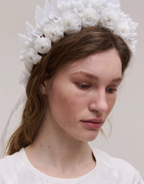 Woman wearing a white floral headpiece against a plain background