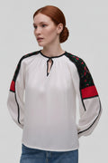Woman wearing a white blouse with black and red accents on a plain background