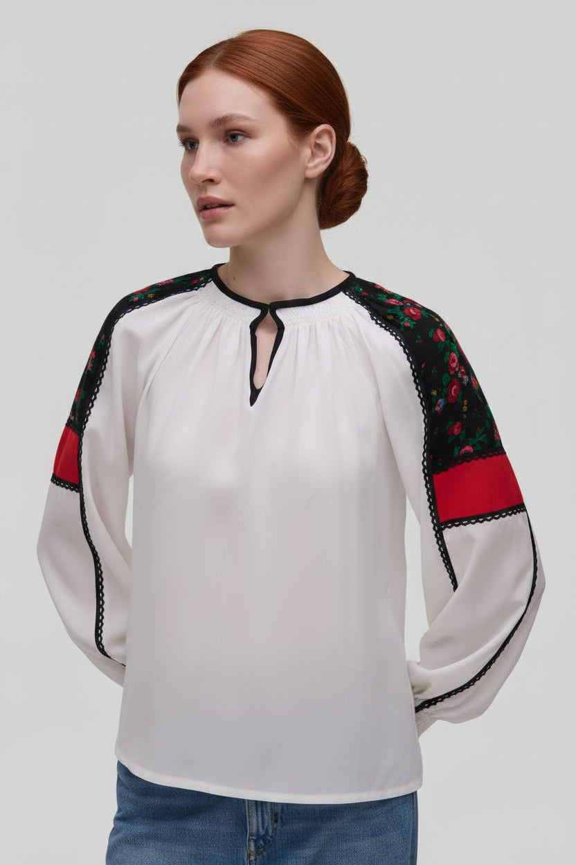 Woman wearing a white blouse with black and red accents on a plain background