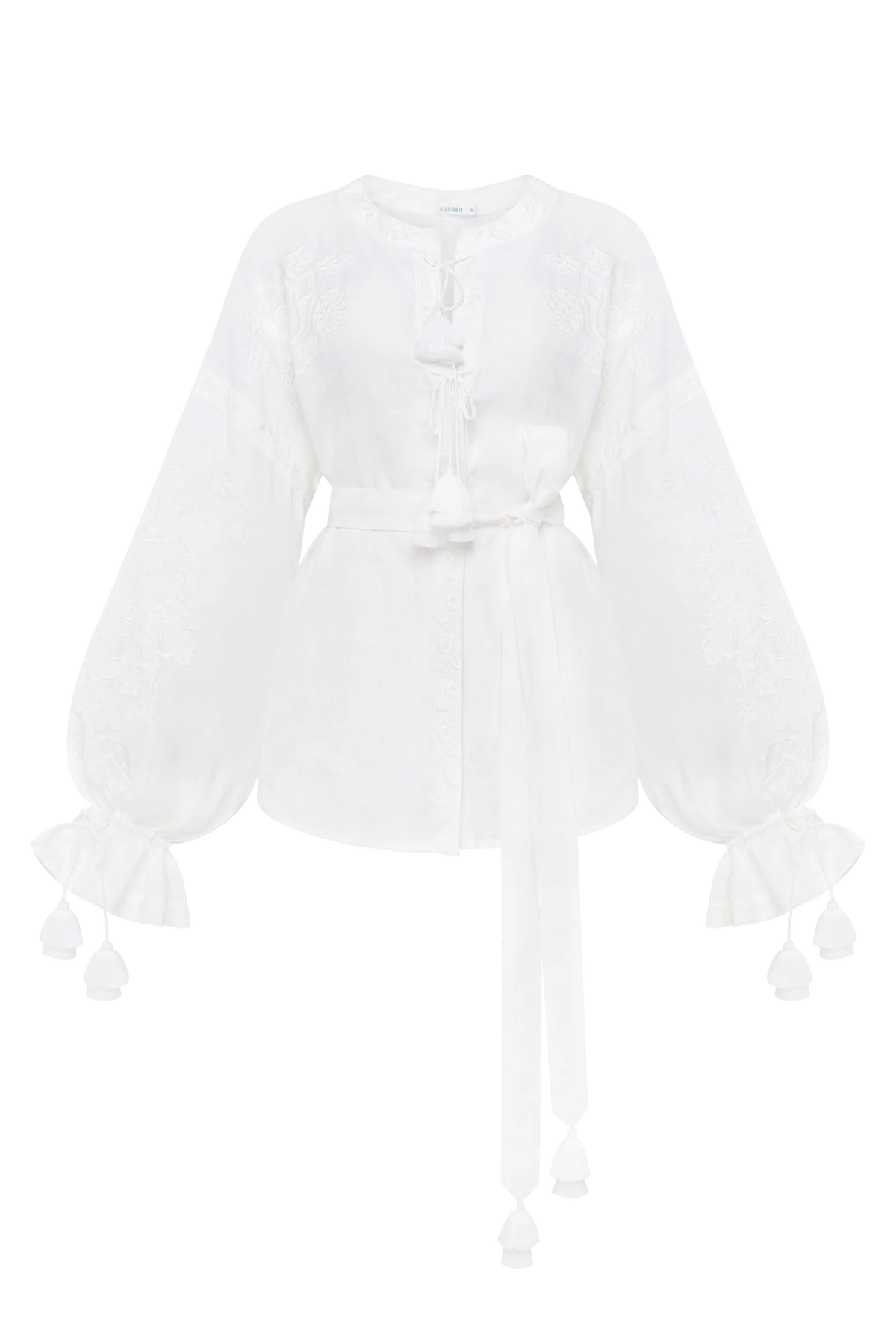 A white long-sleeve blouse with intricate lace embroidery, a tie-neck detail, a matching waist tie, and ruffled cuffs with tassel accents. Annabo designer, Blouse Roumaine Shop