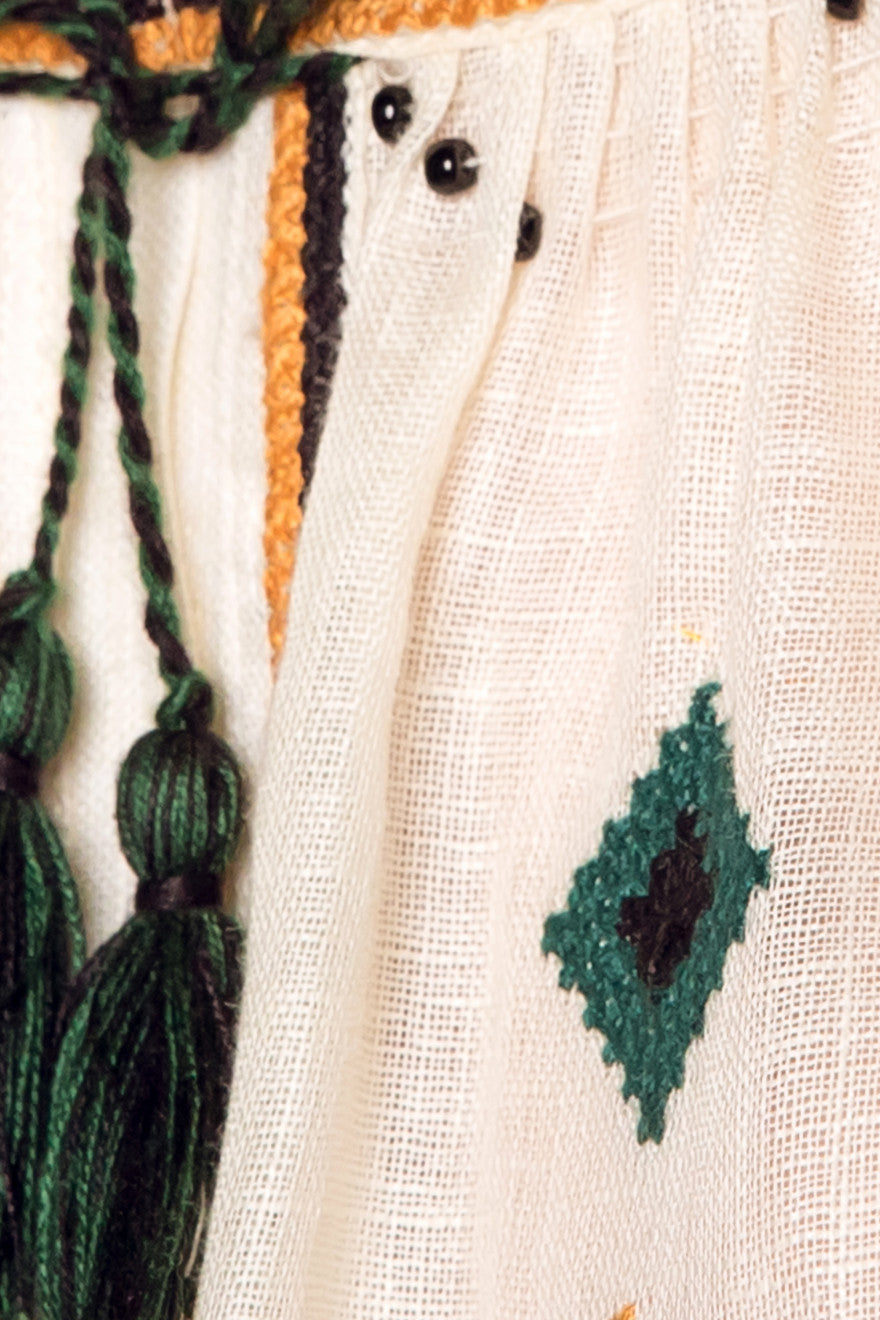 Close-up of a textured fabric with green embroidery and tassels.