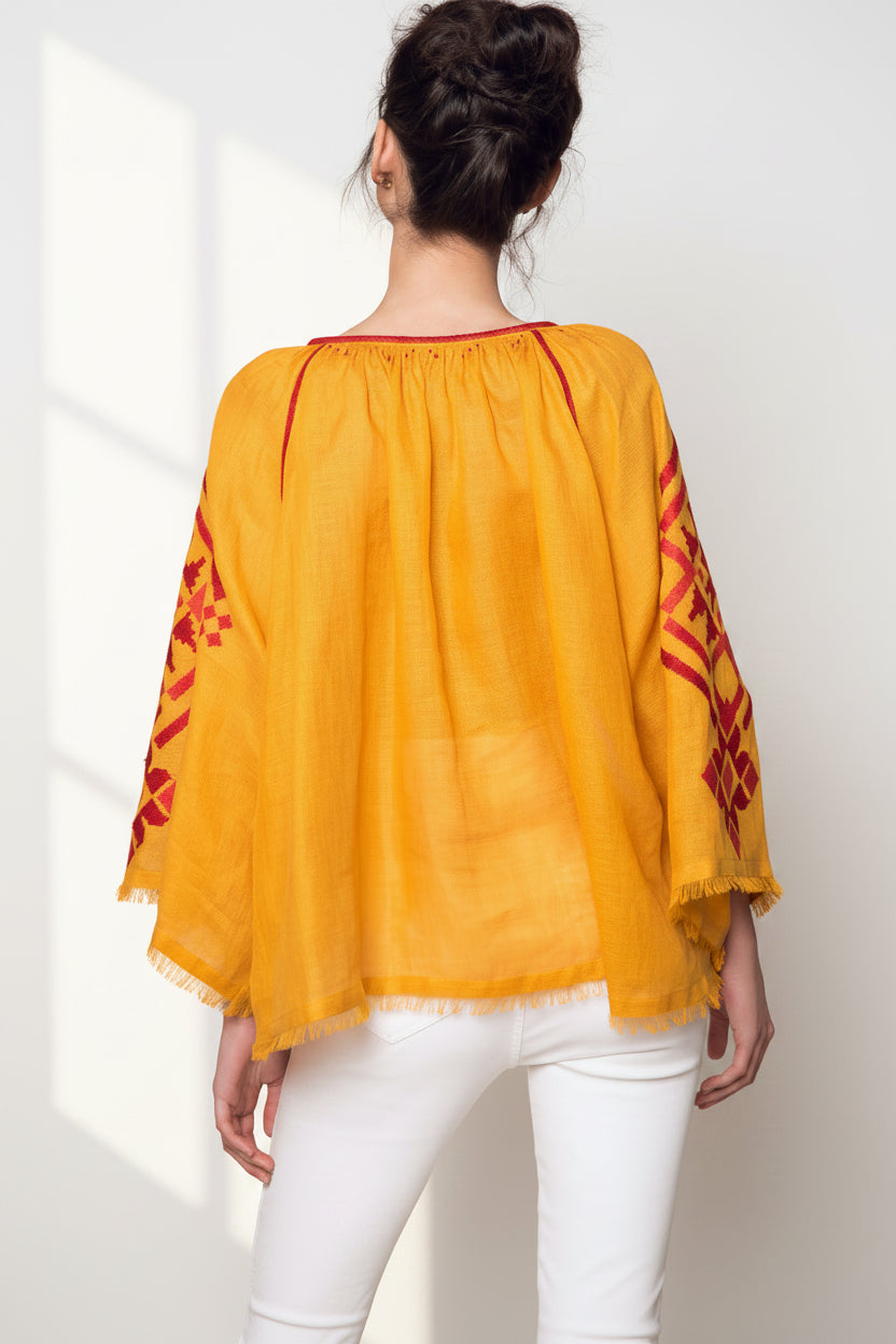 Yellow blouse with red patterns on sleeves worn by a person against a beige background