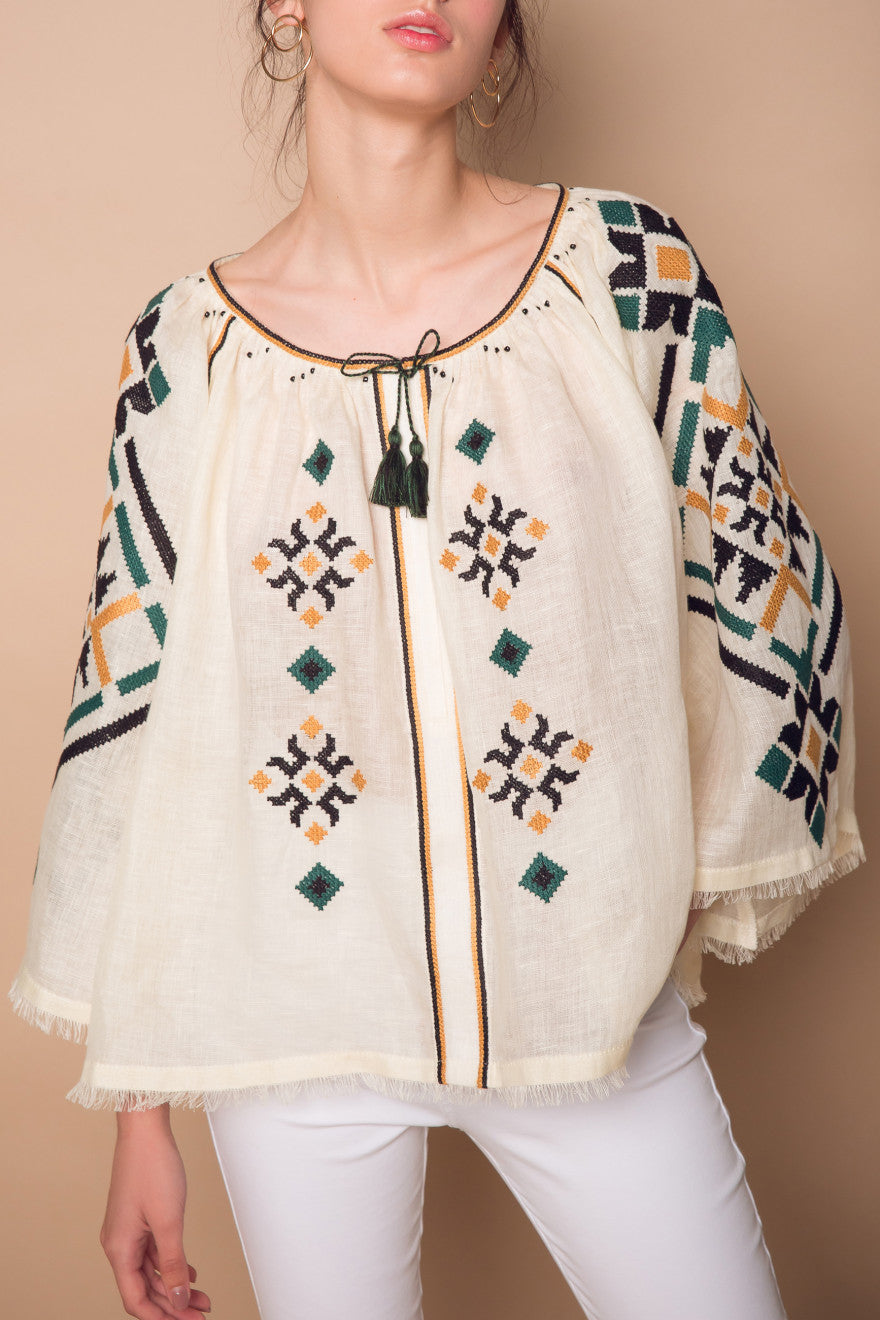 Woman wearing a cream-colored embroidered top with geometric patterns on a beige background