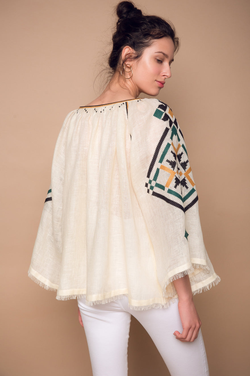 Woman wearing a cream-colored top with geometric patterned sleeves against a beige background