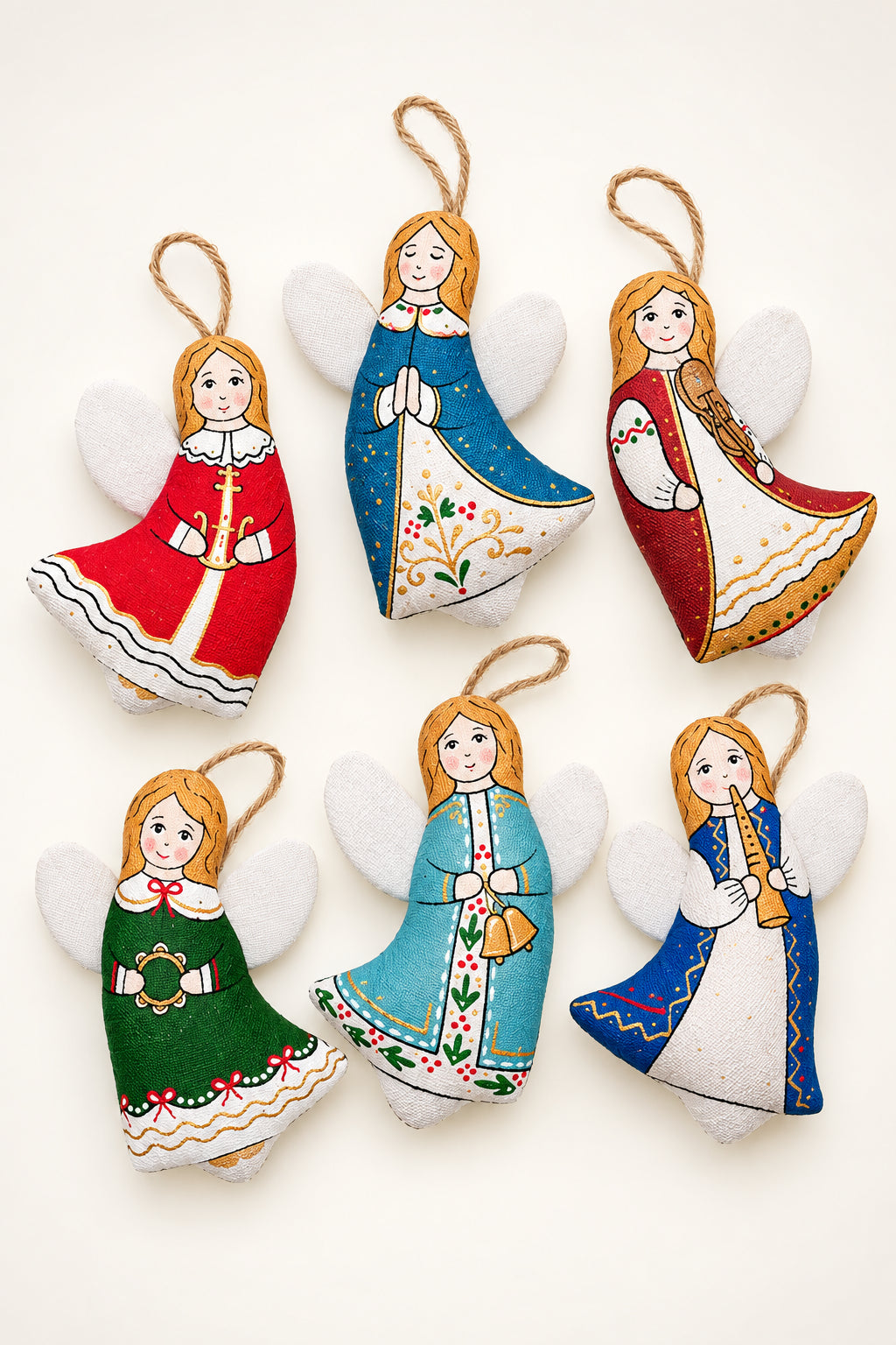 Six hand-painted felt Christmas angel ornaments in various traditional folkloric outfits, arranged on a split green and yellow background with pine branches.
