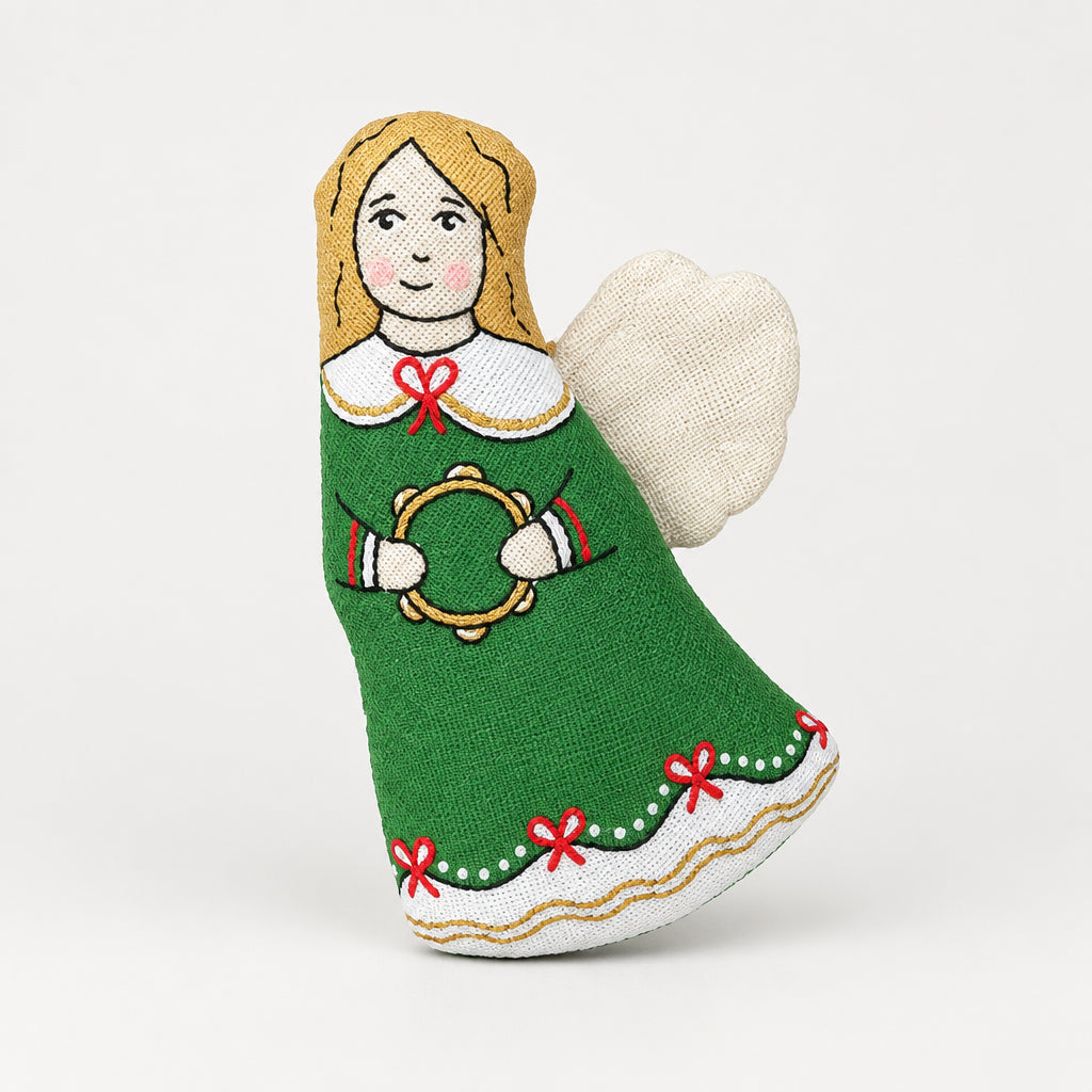 A handmade Christmas stocking ornament featuring a stitched figure of a woman in a green dress holding a wreath, surrounded by holiday decorations including pine branches, red berries, walnuts, and star-shaped cookies on a light gray wooden surface.