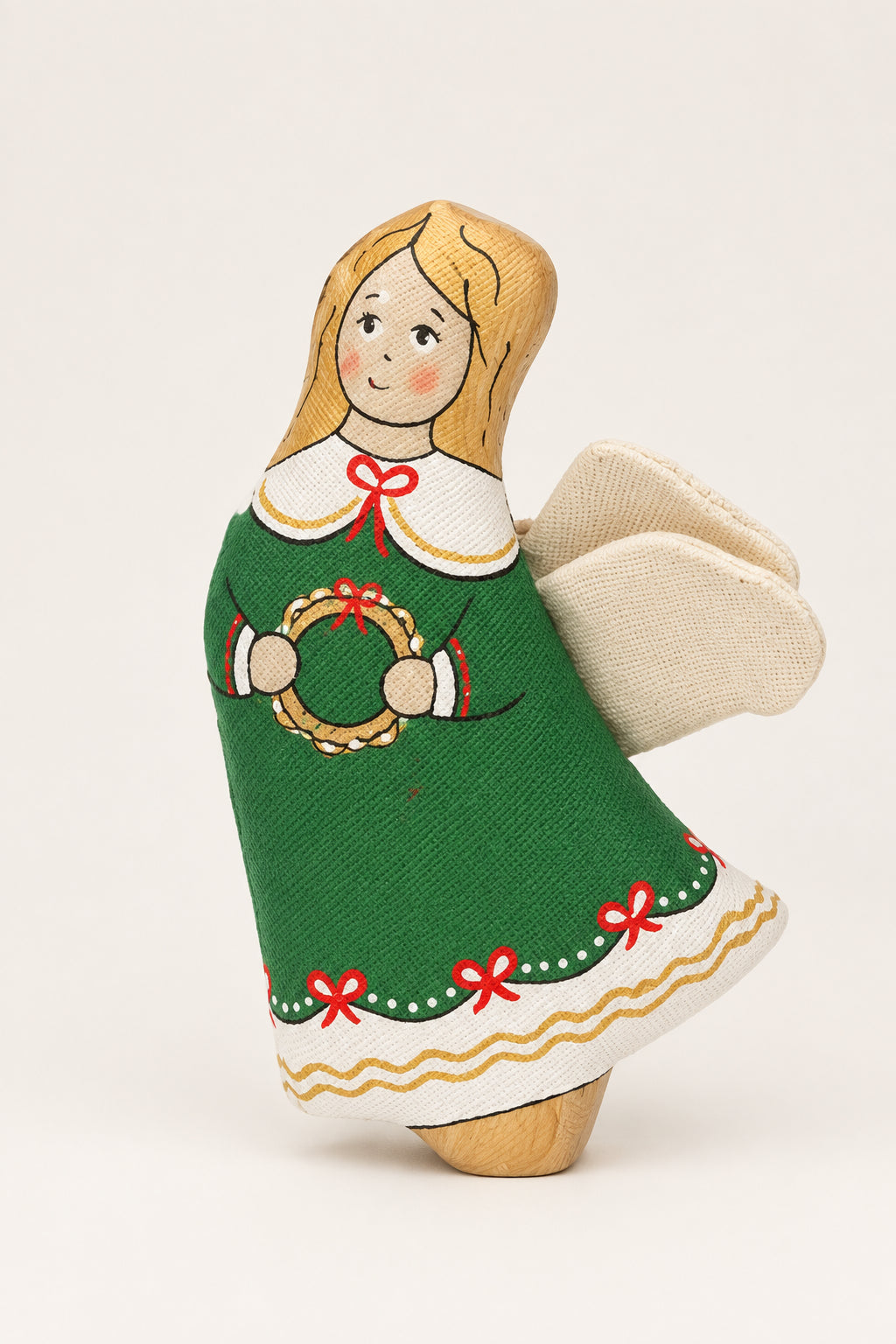 A small handmade fabric angel ornament with blonde hair, a green dress, and white wings, posed in the snow outdoors.