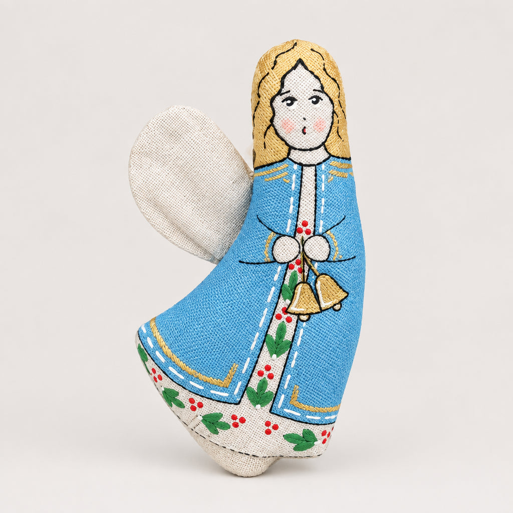 A handmade fabric Christmas angel ornament styled in a flat-lay arrangement with pine branches, red berries, star-shaped cookies, walnuts, and a gold star on a light gray background.