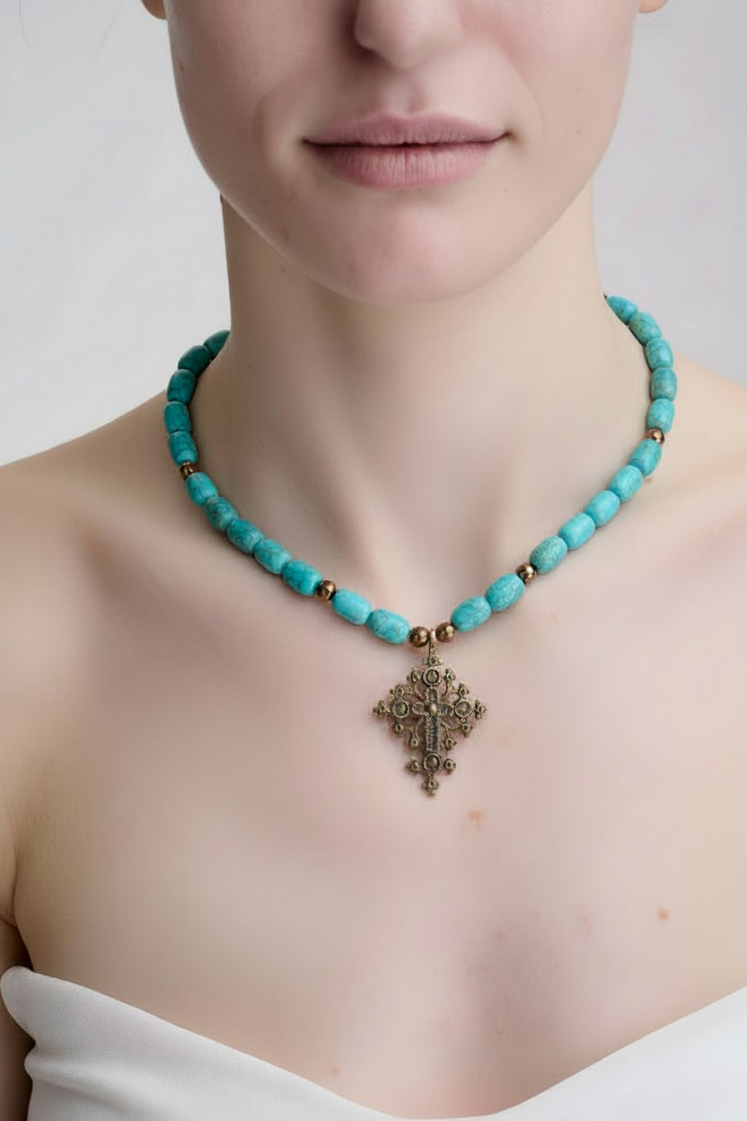 Turquoise beaded necklace with a decorative cross pendant on a plain background