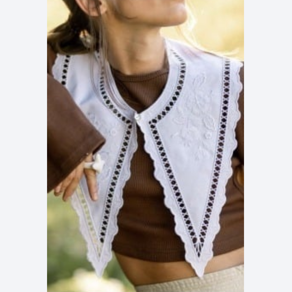 Woman wearing a brown top with a white lace trim  collar cardigan outdoors.