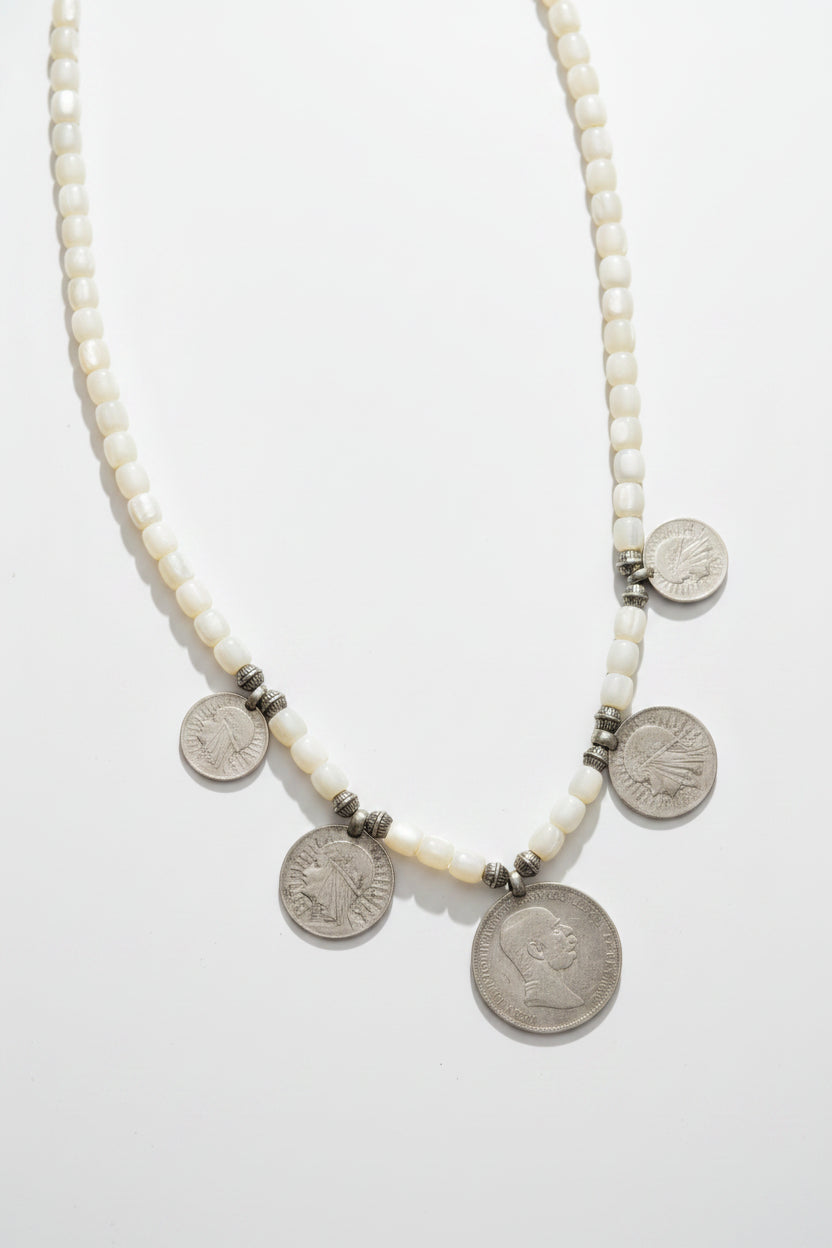 A beaded necklace with white round beads and several silver coin charms, traditional heritage jewlery