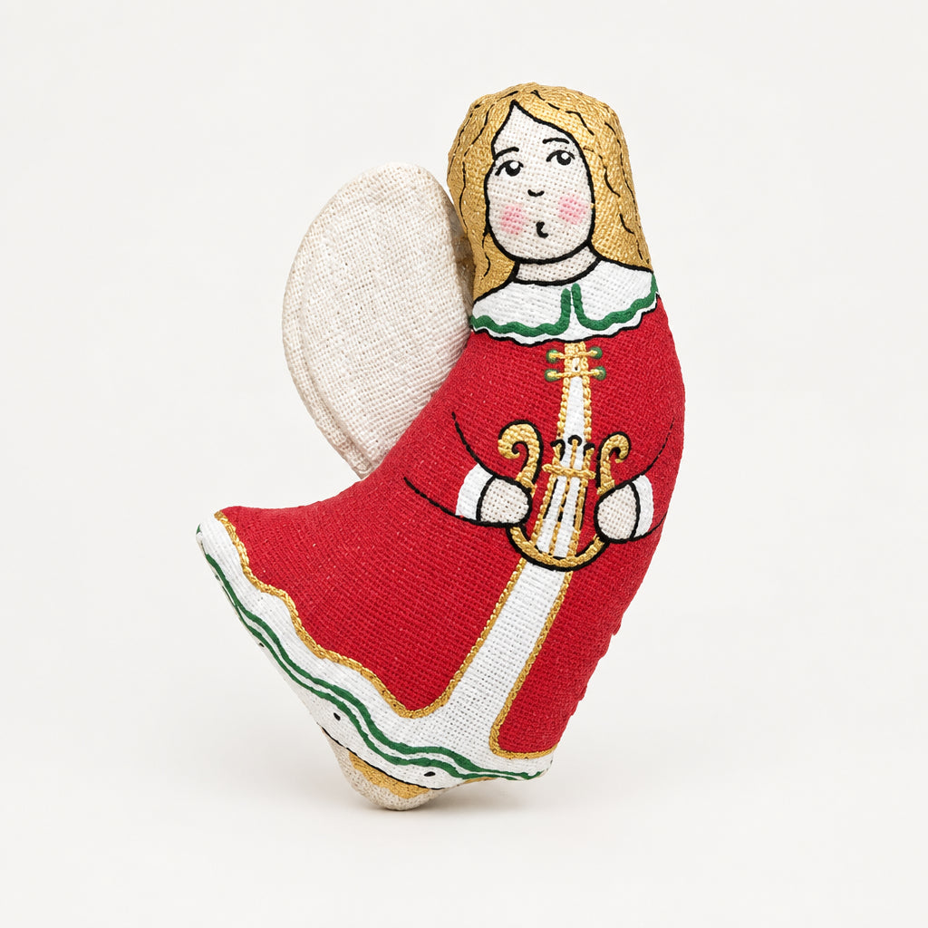 A Christmas angel-shaped cookie decorated with red, white, and green icing, surrounded by holiday decorations including pine branches, red berries, gold star ornaments, and star-shaped cookies on a light gray wooden surface.