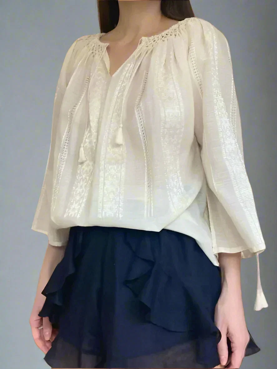 A woman wearing a traditional Romanian blouse in ivory, featuring long sleeves and a honeycomb-pleated collar, paired with a dark skirt.