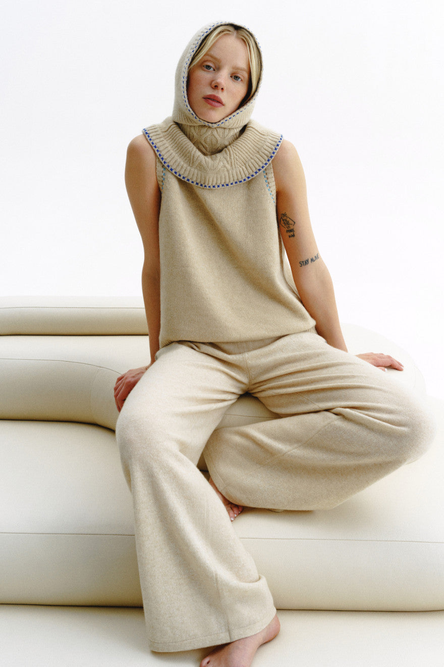 Woman wearing a beige knitted outfit sitting on a white couch.