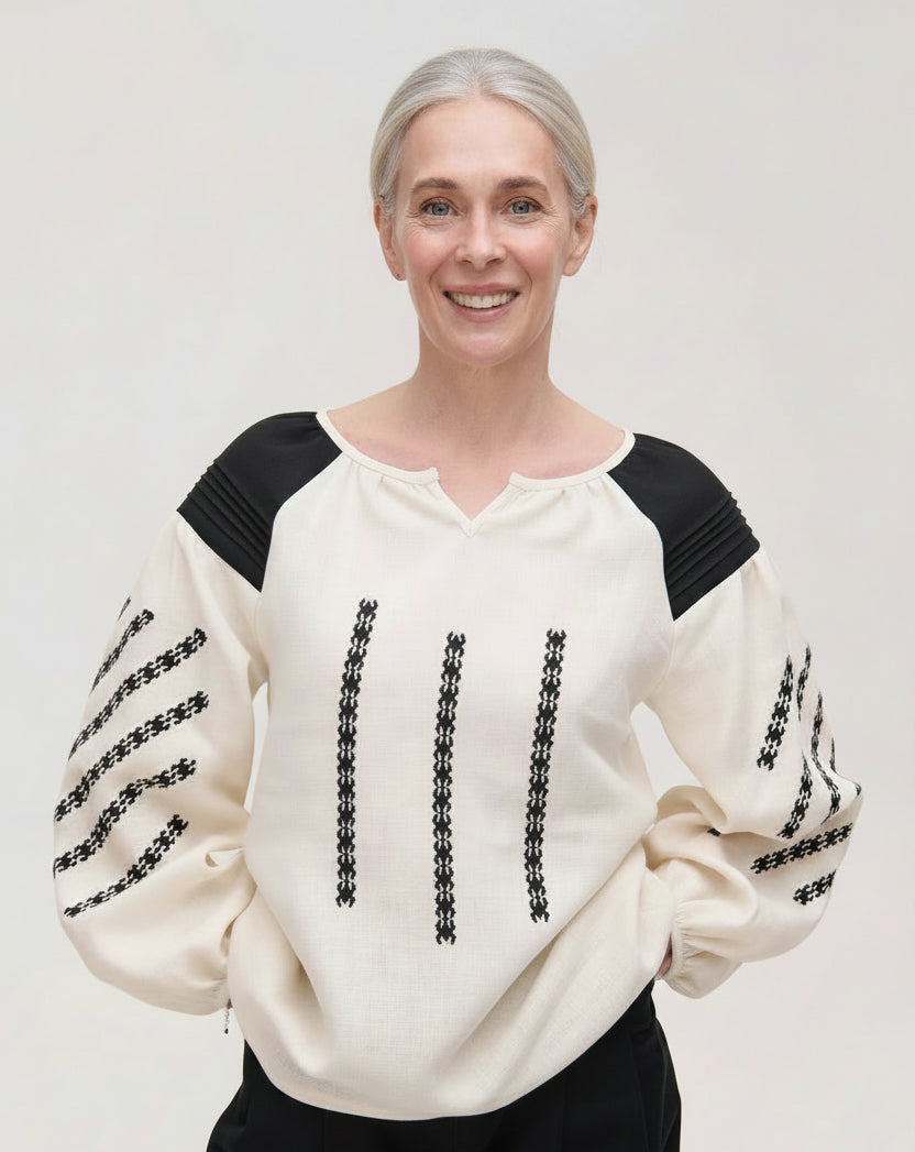 Woman wearing a cream sweater with black accents on a plain background