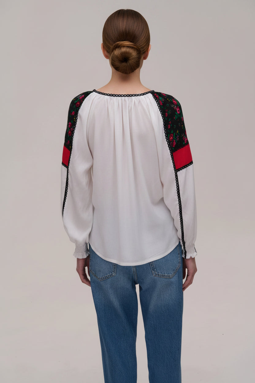 Person wearing a white blouse with embroidered sleeves and blue jeans on a plain background