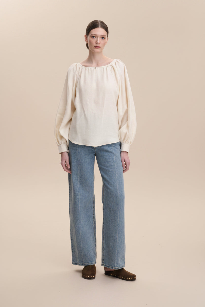 Woman wearing a beige blouse and blue jeans on a white background