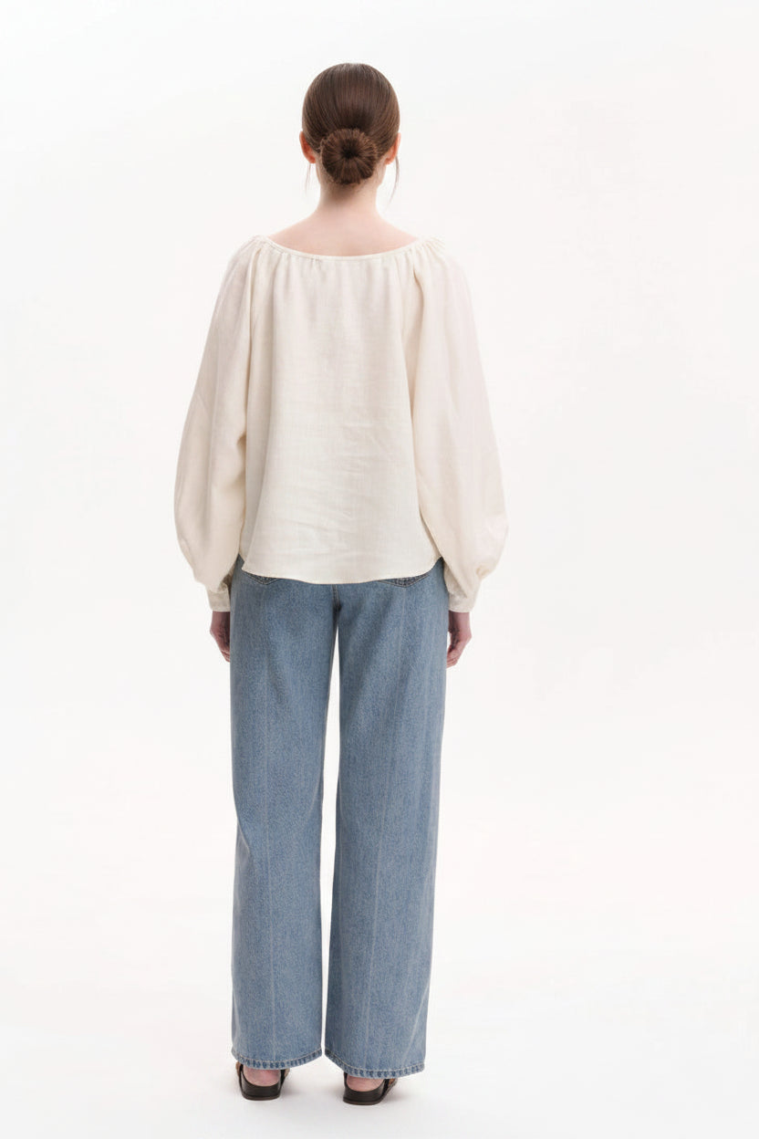 Person wearing a cream blouse and blue jeans on a white background