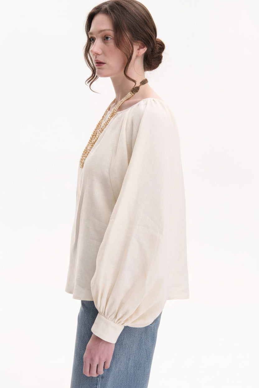 Woman wearing a cream-colored blouse with a gold neckline on a white background