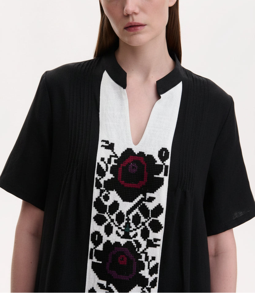 Woman wearing a black cardigan with a white panel featuring black floral patterns on a plain background