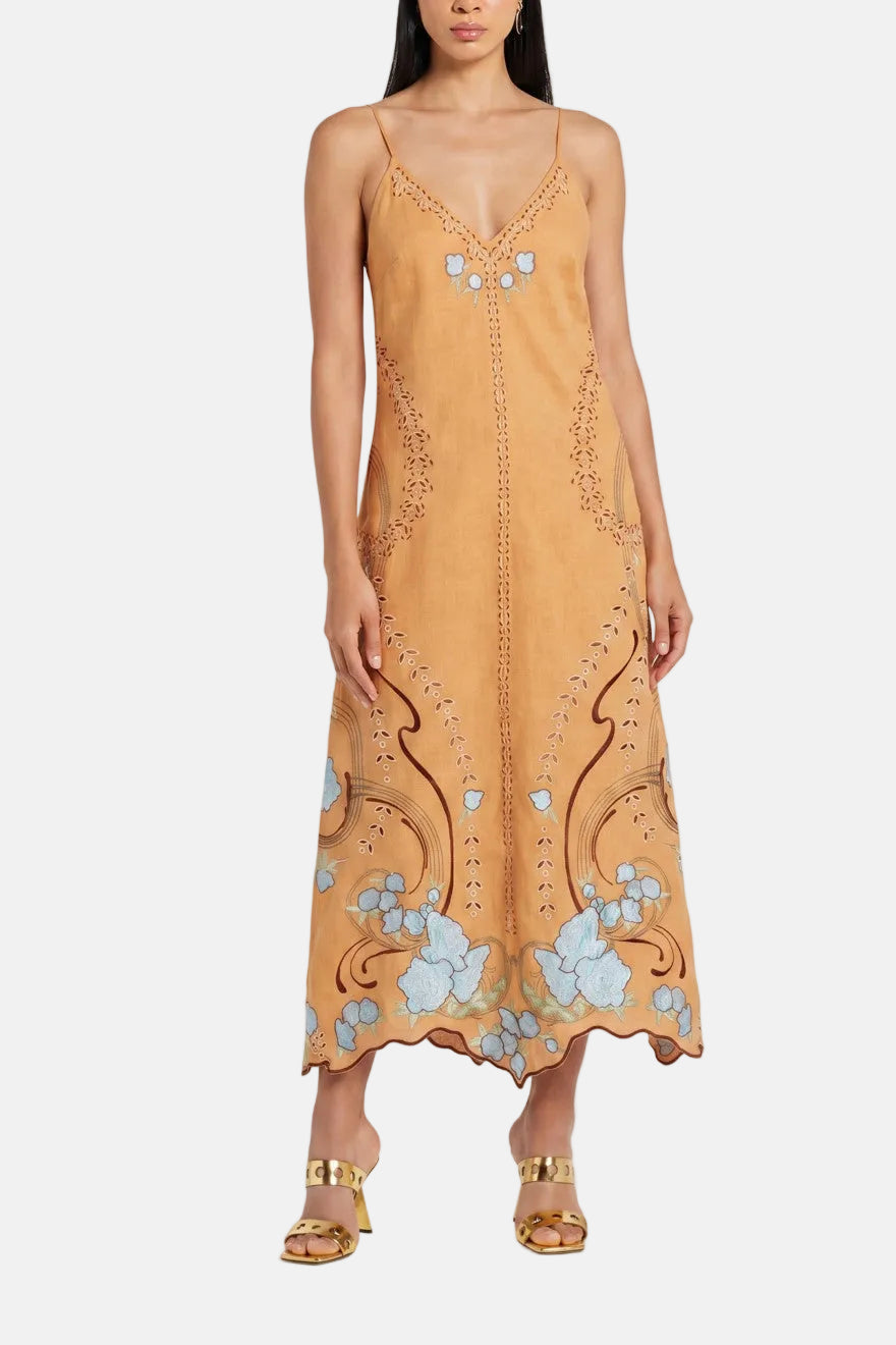 Woman wearing a tan slip dress with floral embroidery on a white background